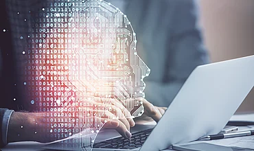 Mann tippt an der Tastatur vor einem Gehirn-Hologramm, Symbolbild zu Kosten und Energiebedarf von KI